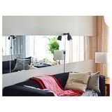 Modernes Wohnzimmer mit schwarzem Sofa, roter Decke, Wandlampen und verspiegelten Wandpaneelen, die ein geräumiges Gefühl schaffen.
