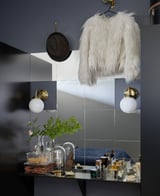 Modernes graues Badezimmer mit verspiegelter Wand, goldenen Lichtern und weißer Jacke neben dem Waschbecken. Pflanzen, Make-up, Pinselset unten.