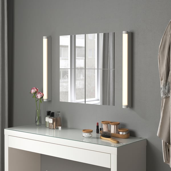 Fazit: ein modernes Badezimmer, das Spiegeltrio BLODLÖNN in Silber, flankiert von beleuchteten Wandlampen, auf einem weißen Waschtisch mit Toilettenartikeln und rosa Rosen.