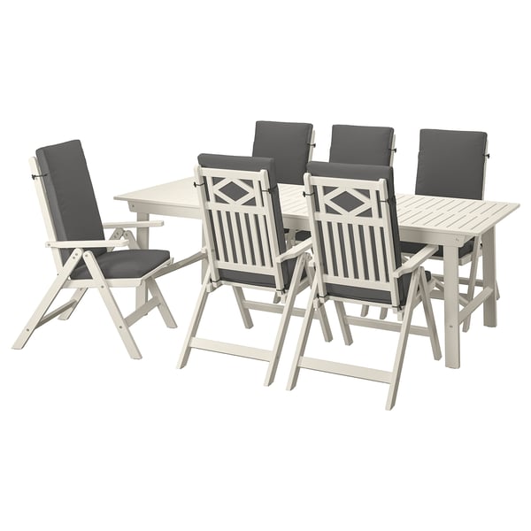 Eine BONDHOLMEN Outdoor-Essgarnitur mit einem Tisch aus weißem Akazienholz und sechs grau gepolsterten Klappstühlen mit Armlehnen.