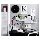 Moderner Schreibtisch mit schwarzem Schreibtisch, weißen Regalen, Uhr, Lampe und Dekorationsgegenständen wie einer roten Figur und einer grünen Pflanze.