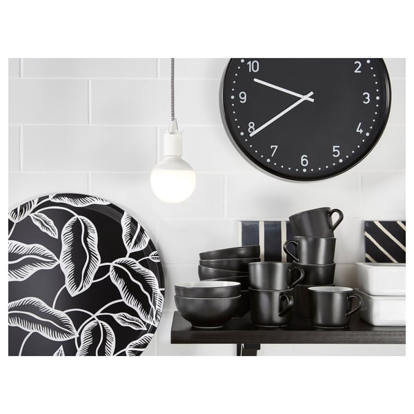 Moderne Küchenszene mit schwarz-weißem Dekor. Enthält eine Wanduhr, ein Holzregal mit schwarzen Tassen und Schalen sowie einen verzierten schwarzen Teller.