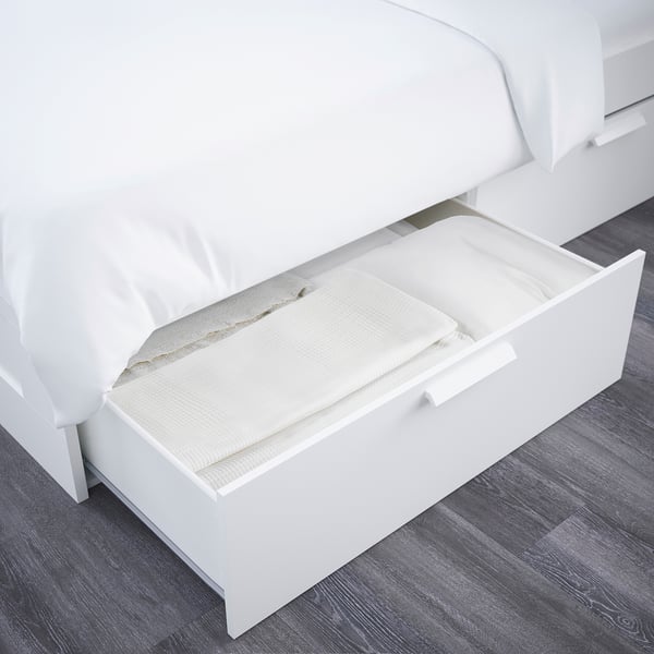 Offenes weißes Bett mit Schublade, in der gefaltete Bettwäsche zu sehen ist. Modernes, platzsparendes Design.