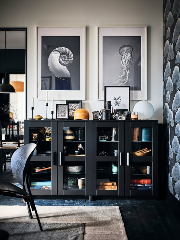 Modernes Wohnzimmer mit schwarzem BRIMNES-Schrank, Glastüren, Ausstellungsdekor, grauem Teppich, schwarzem Stuhl, Lampe.