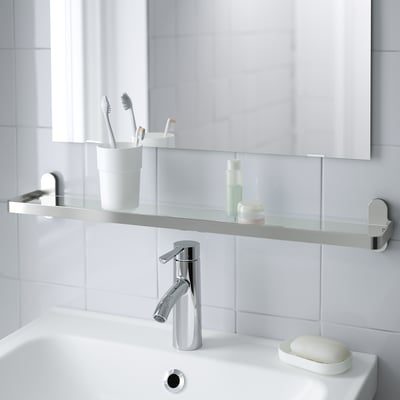 Ein modernes Waschbecken mit einem verchromten Wasserhahn und einer Glasablage für Toilettenartikel.