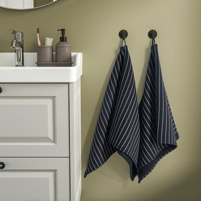 Modernes Badezimmer mit grünen Wänden, weißem Schrank, gestreiftem Handtuch und Waschbecken.