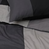 Weiches, gefaltetes graues Bettwäsche-Set mit glattem Stoff, mit glatten schwarzen Besätzen, ordentlich angeordnet.