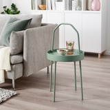 Ein grüner Beistelltisch von BURVIK neben einem grauen Sofa. Der runde Tisch hat einen Griff und eine geringe Größe und bietet Platz für ein Glas und eine Schale.