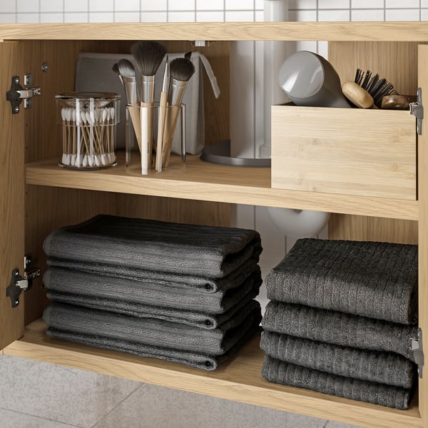 Holzschrank mit dunklen Handtüchern und Make-up-Pinseln; Stauraum im Badezimmer.