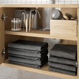 Holzschrank mit dunklen Handtüchern und Make-up-Pinseln; Stauraum im Badezimmer.