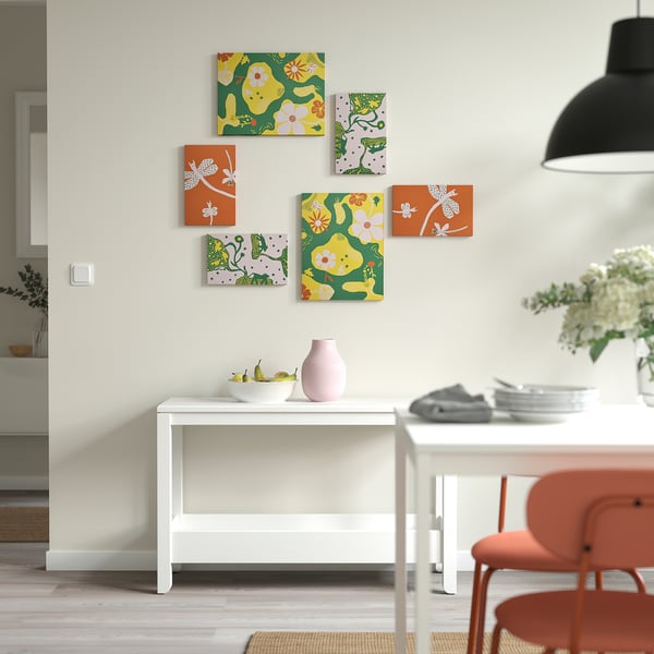 Bunte, von der Natur inspirierte Kunst in Orange und Grün an der Wand über dem weißen Tisch mit rosa Vase und Obst.