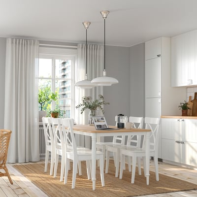Moderne weiße Essgarnitur mit 6 Stühlen, rechteckigem Tisch, sanfter Beleuchtung und großem Fenster.