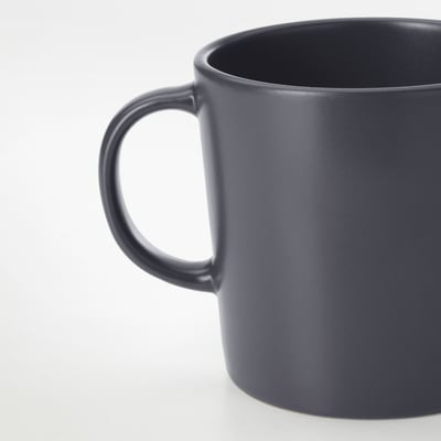 Dunkelgrauer, matter Becher mit stabilem Henkel, der auf einer glatten Oberfläche ruht.