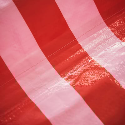 Ein rot-weiß gestreiftes Zelt. Das Zelt ist quadratisch geformt und mit einem reflektierenden Material versehen.