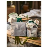 Zwei Aufbewahrungsboxen aus Stoff mit Bären- und Tupfenmotiven auf einem Holzregal, in denen Babyartikel wie Windeln, Schnuller, Kleidung und Spielzeug aufbewahrt werden.