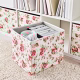 Blumen-Aufbewahrungsbox auf dem Regal mit Kopfhörern und Kabeln, Teil der Kallax-Einheit.