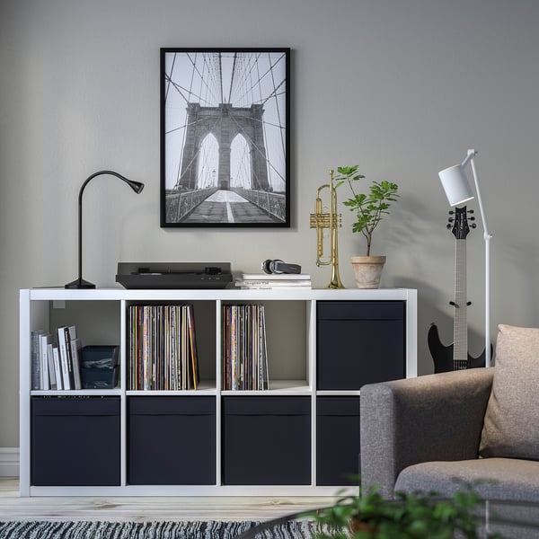 Modernes Wohnzimmer mit DRÖNA-Stauraum, Schallplatten, Büchern, Trompete, Pflanze, Lampe, Gitarre und Brooklyn-Bridge-Foto.