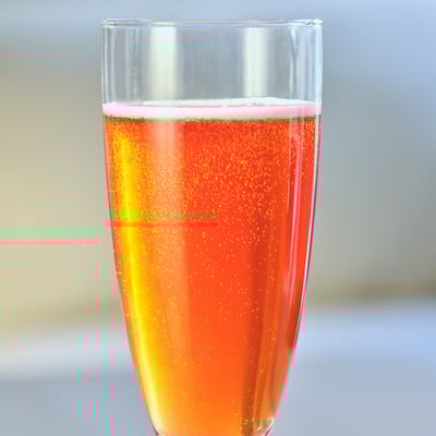 Klarglasbecher mit Orangensprudelgetränk, wahrscheinlich alkoholfrei, durch Sonnenlicht sehend.