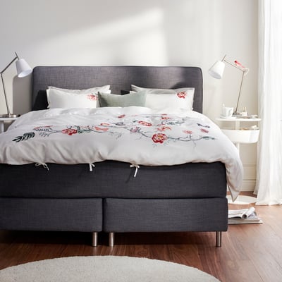 Elegantes, modernes Schlafzimmer mit einem grauen DUNVIK-Bett, weißer Blumenbettwäsche, passenden Nachttischen und Lampen.