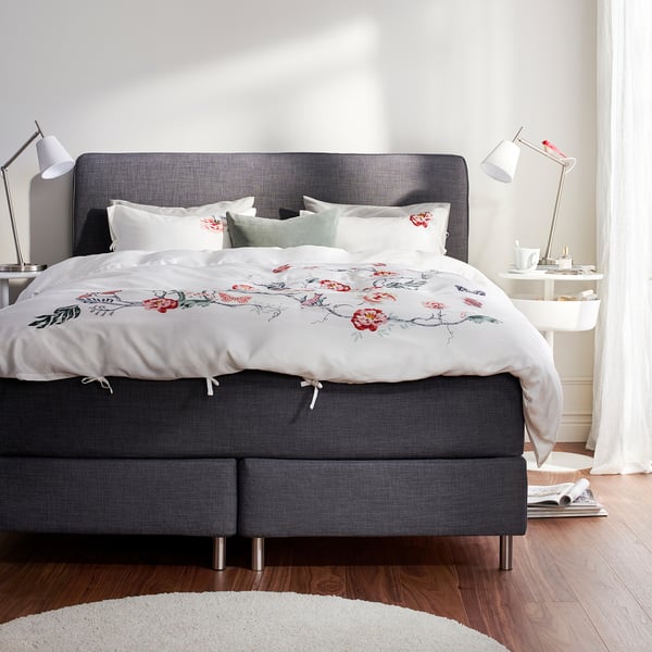 Abnehmbare Bettwäsche auf grauem Bett, weißer Teppich, zwei Lampen, Holzboden, ruhiges Zimmer.