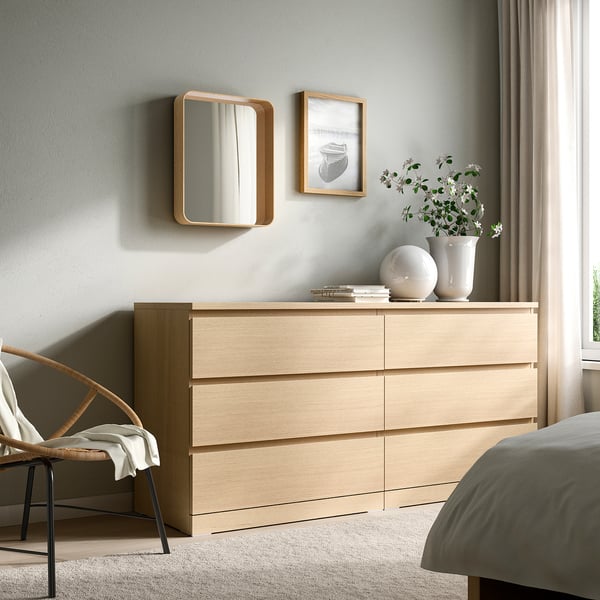 Holzkommode mit DVÄRGSYREN-Spiegel, großem Bett, Stuhl und Handtuch.