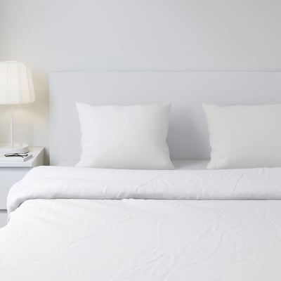 Weiße DVALA-Bettwäsche mit Baumwollkissenbezügen auf einem minimalistischen Bett, ruhige Atmosphäre, kleine Lampe.