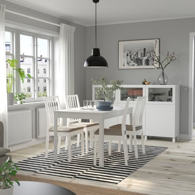 Modernes Esszimmer mit weißem EKEDALEN-Tisch und Stühlen, gestreiftem Teppich, großem Fenster, Pendelleuchte, Pflanze, Vase und gerahmtem Stadtfoto.