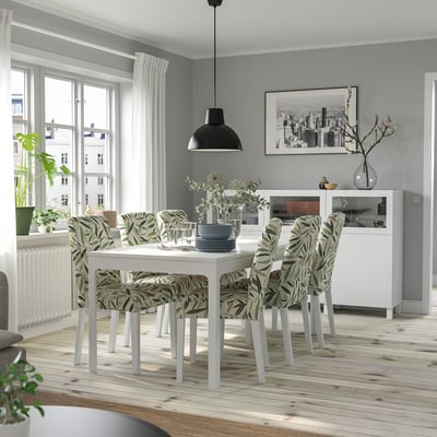 Modernes Esszimmer mit weißem Tisch, grünen Stühlen, Stadtblick, Schwarzlicht, grauen Tellern und einem Sideboard mit Vase.