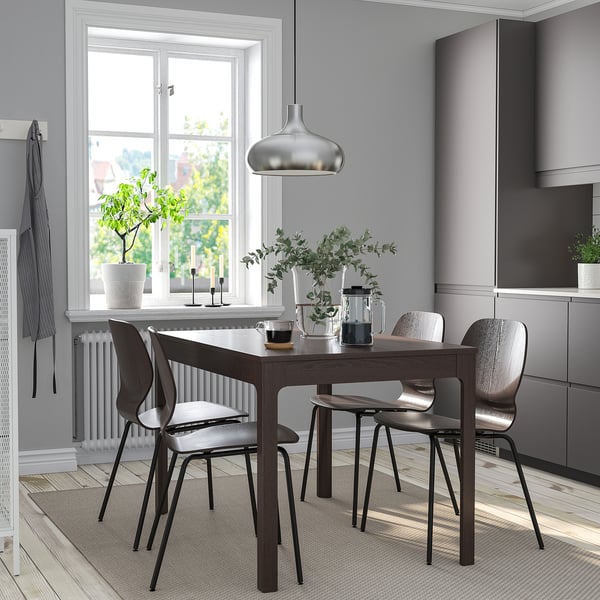 Modernes Esszimmer mit ausziehbarem grauem Tisch, Stühlen, Metallanhänger, Pflanzen, Kerzenhalter, Teppich.
