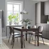Modernes Esszimmer mit ausziehbarem grauem Tisch, Stühlen, Metallanhänger, Pflanzen, Kerzenhalter, Teppich.
