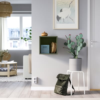 Innenraum mit grünem EKET-Schrank, Kaktus, Rucksack, Kranmalerei, grauen Wänden, Holzböden und großem Fenster.