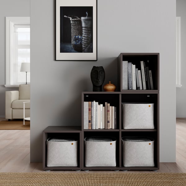 Dunkelbraunes modulares Regal mit Stoffbehältern und Büchern, mit Dekor gestaltet, vor einer grauen Wand mit einem gerahmten Bild.