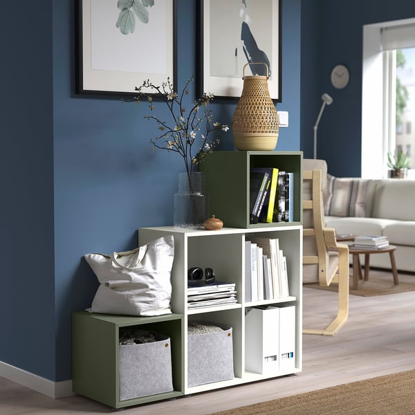 Modernes Wohnzimmer mit grünem EKET-Regal, in dem Bücher, Vasen und Kissen vor graublauer Wand ausgestellt sind.