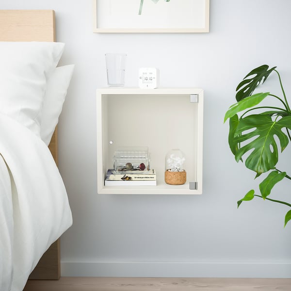 Minimalistisches Schlafzimmer mit weißem EKET-Würfelregal zur Aufbewahrung und Präsentation, das eine Uhr, Pflanzen und Accessoires zeigt und in der Nähe eines Bettes platziert ist.