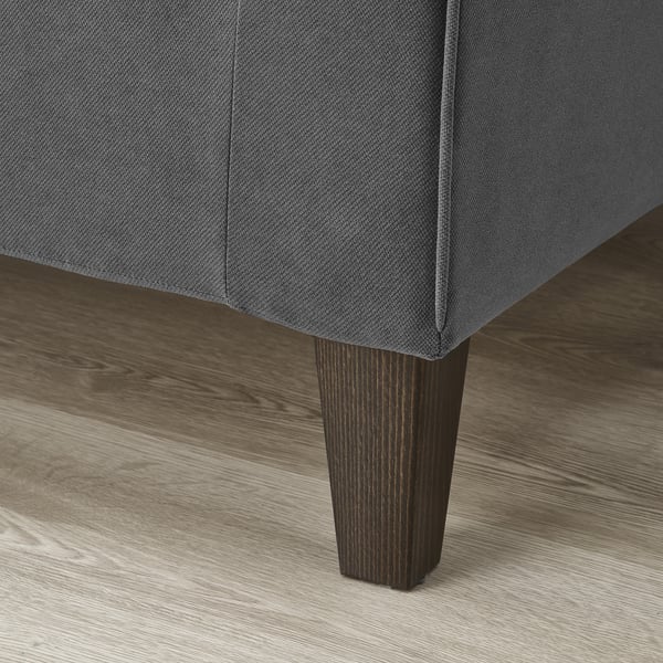Nahaufnahme des Sofas: dunkelgraue Polsterung, spitz zulaufende Holzbeine, polierter Boden.
