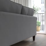 Graues Sofa mit dunklen Holzbeinen in der Nähe eines großen Fensters; Bietet sowohl Komfort als auch Stil.