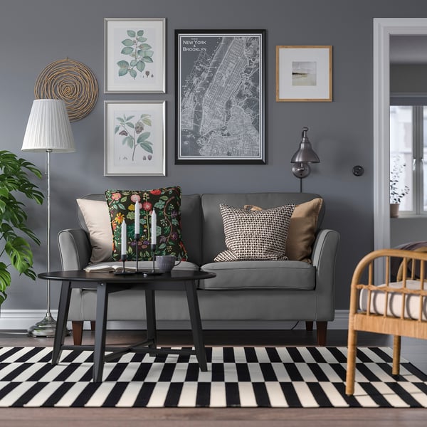 Modernes Wohnzimmer mit grauem EKHOLMA-Sofa, schwarz-weiß gestreiftem Teppich, Pflanzen und Wandkunst.
