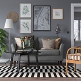 Modernes Wohnzimmer mit grauem EKHOLMA-Sofa, schwarz-weiß gestreiftem Teppich, Pflanzen und Wandkunst.