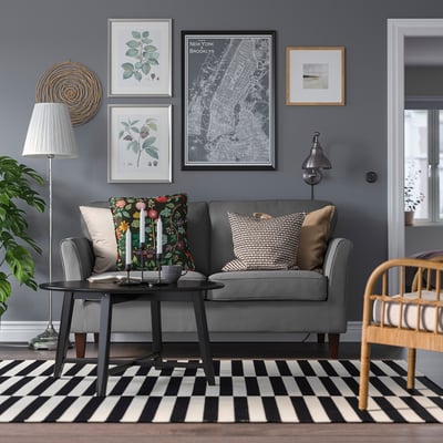 Modernes Wohnzimmer mit grauem EKHOLMA-Sofa, schwarz-weiß gestreiftem Teppich, Pflanzen und Wandkunst.