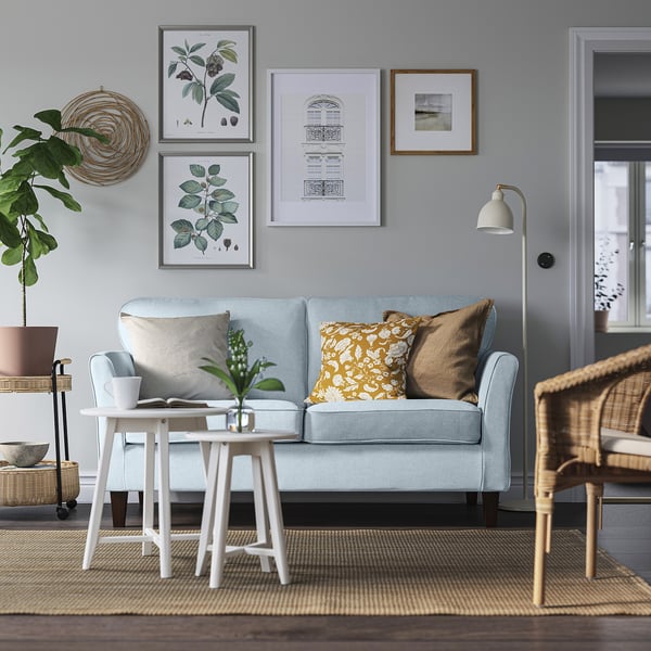 Modernes Wohnzimmer mit blauem EKHOLMA-Sofa, Couchtisch, Pflanze und Wandkunst.