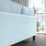 Hellblaues Sofa mit Holzbeinen, in der Nähe von Fenstern und Pflanzen, bietet Komfort mit Taschenfedern und abnehmbarem Bezug.