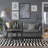 Gemütliches, modernes Wohnzimmer mit grauem EKHOLMA-Sofa, schwarzem Couchtisch, schwarz-weißem Teppich und Wandkunst. Das Sofa passt gut unter große Kunstdrucke.