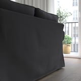 Schwarzes Sofa mit dicken Kissen in der Nähe eines Fensters, das Komfort und Halt bietet.
