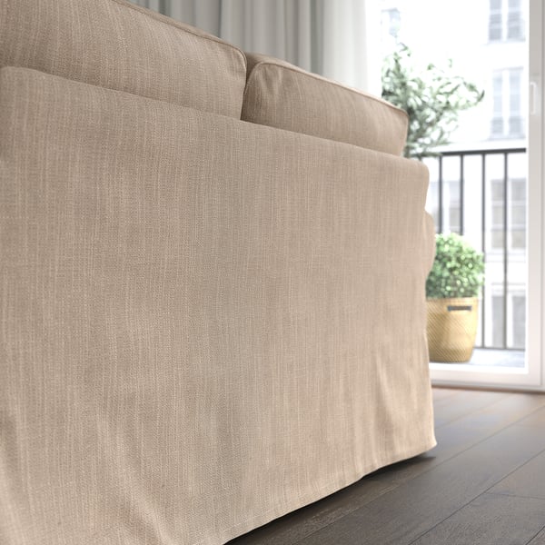 Neutrale Couch mit dicken Kissen in der Nähe eines großen Fensters, das natürliches Licht in einen gemütlichen Raum mit einer Topfpflanze in der Nähe bringt.