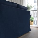 Dunkelblaues Sofa mit dicken Kissen, das in der Nähe eines Fensters mit einer Pflanze platziert ist und Komfort und Stil bietet.