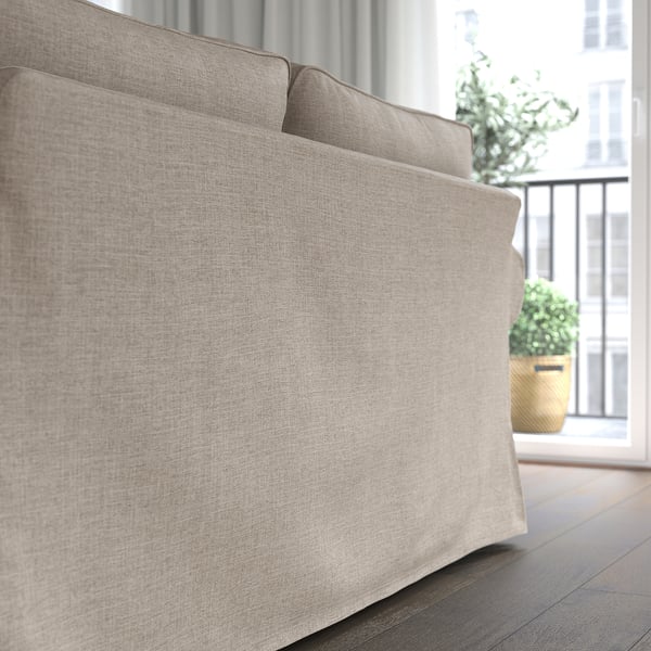 Beige gepolstertes Sofa in der Nähe des Fensters mit Pflanze. Weiche, wendbare Kissen für gemütliches Sitzen.