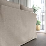 Beige gepolstertes Sofa in der Nähe des Fensters mit Pflanze. Weiche, wendbare Kissen für gemütliches Sitzen.