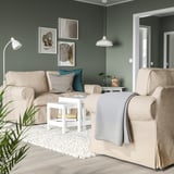 Modernes Wohnzimmer mit beigen EKTORP-Sofas, grünen Wänden, weißen Möbeln und abstrakter Wandkunst.