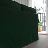 Dunkelgrünes EKTORP-Sofa in der Nähe des Fensters, mit üppigen Pflanzen draußen.