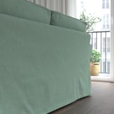 Ein gemütliches, türkisfarbenes EKTORP-Sofa in der Nähe eines Fensters, das eine bequeme, einladende Sitzgelegenheit mit dicken Kissen bietet.